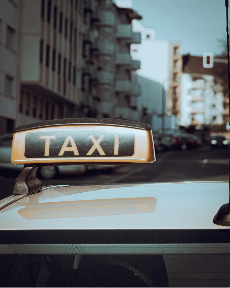 Close-up of a taxi sign on a car with city buildings in the background.